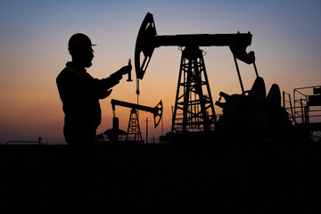 Silhouette of a chemical engineer taking a sample of crude oil against the background of oil pumps.
