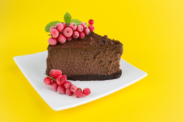 A piece of chocolate cheesecake on the white plate on the yellow background. Closeup. Copy space.