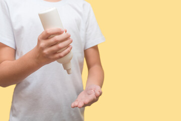a child in a white T-shirt on a yellow background treats his hands with a spray from a bottle against the virus