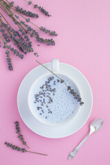 Fototapeta na wymiar Top view of lavender moon milk in the white cup on the pink surface. Location vertical.