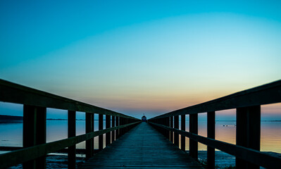 Wooden pier by the ocean at sunset, view down along the boardwalk.