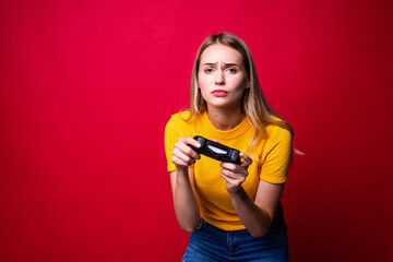 Young blonde gamer woman using gamepad playing video games over red background