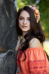 Beautiful Slavic woman in an orange ethnic dress and a wreath of flowers on her head. Beautiful natural makeup. Portrait of a Russian girl