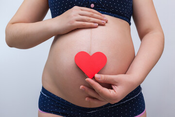 A pregnant woman holds a heart symbol against the background of her stomach
