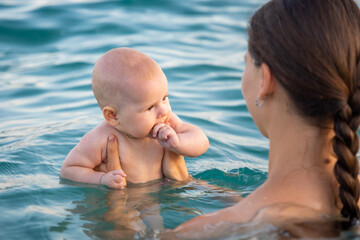 Beautiful young woman with her daughter little baby girl swimming and relaxing in the sea at sunset time