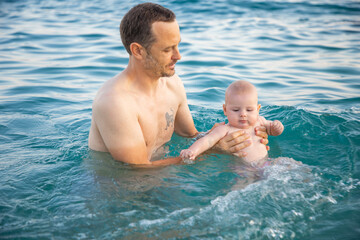 Father with her daughter little baby girl swimming and relaxing in the sea at sunset time