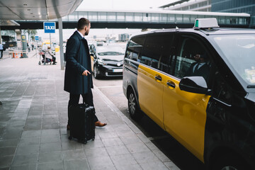Businessman with luggage catching taxi next to airport - obrazy, fototapety, plakaty