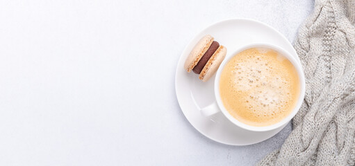 Horizontal banner with knitted scarf, coffee and chocolate macaron on stone background. Cozy autumn composition. Flat lay, top view