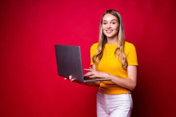 Naklejka premium Portrait of smiling young woman holding, working on laptop pc computer isolated on red background.