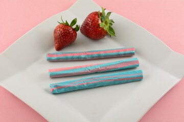 Strawberry milkshake chew candy sticks and fresh strawberries on white snack plate