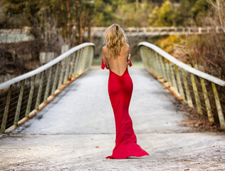 Beautiful and sexy blonde woman in red long dress on bridge. 