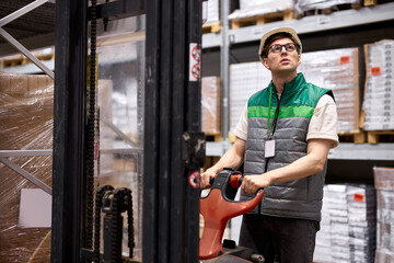 Fototapeta na wymiar confident warehouse worker with hand pallet truck or pallet jack and the shipment in store, caucasian male in uniform at work