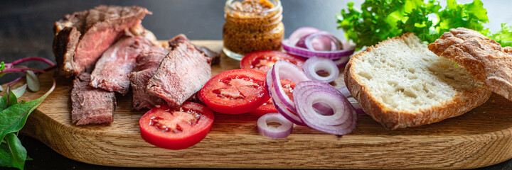 meat sandwich and vegetables burger loaf of bread, tomato, lettuce, medium or rare steak on the table serving size top view copy space for text food background rustic