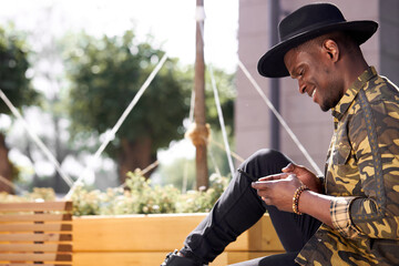 handsome dark-skinned man chatting with friend outdoors, young male look at smartphone and smile