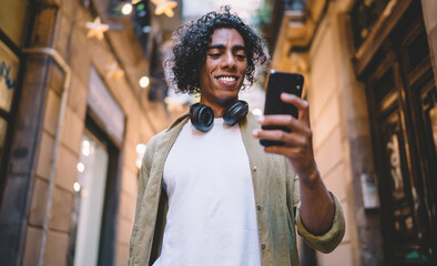 Positive black man with headphones using phone outside