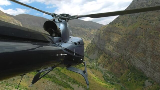 The helicopter flies through the gorge of the high mountains. View from the tail of the helicopter in 4K