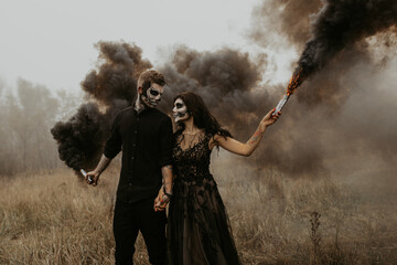 Couple with dark skull makeup with black smoke bombs in their hands.