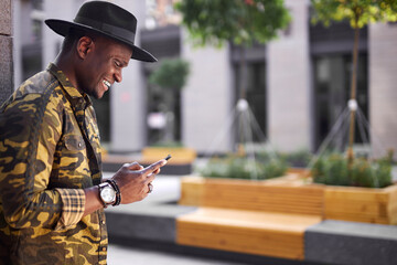 good-looking black male use smartphone while he is walking outdoors, stylish guy chatting with girlfriend