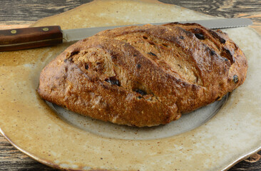 Loaf of cranberry walnut bread with bread knife on large serving plate on table