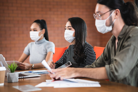 Group of young Asian business man and woman wearing face mask during working or meeting together in office for prevent coronavirus infection during covid-19 pandemic. New normal business concept.