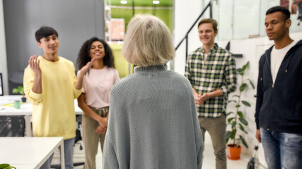Fototapeta premium Cheerful young team greeting new employee, Back view of aged woman, senior intern at her new job in the modern office