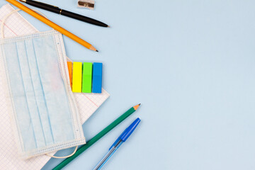 School supplies with a mask on a blue background. View from above. Place for text. Epidemic. Education concept.