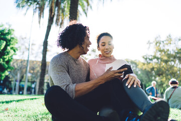 Positive young diverse couple relaxing on lawn in park