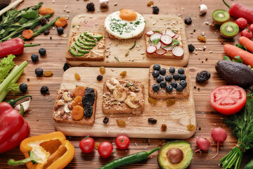 Close up of protein toast with various delicious toppings on cutting board, Healthy breakfast ideas with vegetables, fruits and greenery on the wooden background