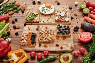 Close up of protein toast with various delicious toppings on cutting board, Healthy breakfast ideas with vegetables, fruits and greenery on the wooden background