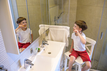 A cute little boy is brushing his teeth with a toothbrush. On a pure white T-shirt in which he is dressed you can make an advertising inscription. The concept of children's health, medicine