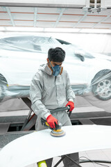 young auto mechanic man buffing and polishing car holding polisher in hand, in repair shop. renew...