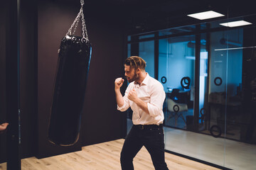Caucasian worker in smart casual clothing punching boxing bag disappointed with miss fortune...