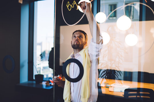 Caucasian businessman making notes of ideas for presentation projecting using modern glass board in coworking space, smart casual employee 30 years old analyzing solutions and created graph charts - Powered by Adobe