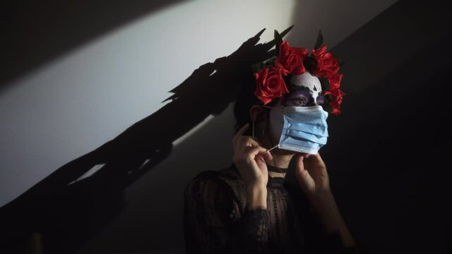 Concepto de Carnaval o Halloween. Mujer asustada con mascarilla anti covid y virus de la pandemia, pintada de calavera mexicana blanca, usa ropa negra en un escenario de miedo 4K