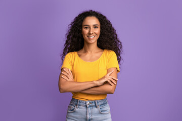 Portrait Of Confident Young Woman Posing With Folded Arms Over Purple Background