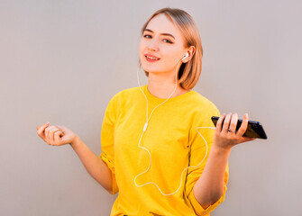 Happy carefree young woman dancing and listening to music from smartphone over grey background