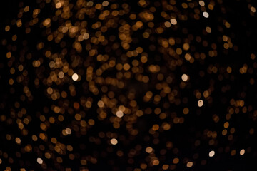 Golden blurry bokeh spots on a black background. Festive background.