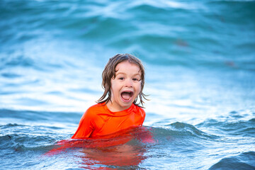 Fototapeta na wymiar Happy kid boy playing and having fun on the beach on blue sea in summer. Blue ocean with wawes. Child boy swimming in sea.