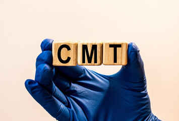 The word CMT which is made from wooden cubes. Hands in a blue glove. Isolated on WHITE background.