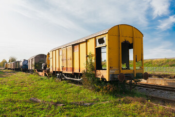 Old yellow train with big holes, rusty and abandoned on the old tracks in the field, on a bright summer day
