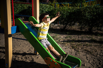 summer, childhood, leisure, friendship and people concept - happy little boy on children playground slid from the hill
