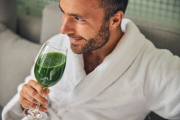 Joyful young man drinking smoothie in spa salon