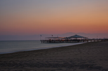 Fototapeta premium Sunset over the massive concrete pier leading to horizon surrounded by Mediterranean sea. Long exposure shot made in Belek, Turkey. August 2020