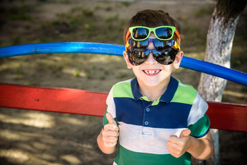 Portrait of a cheerful boy child in several sunglasses outdoors.