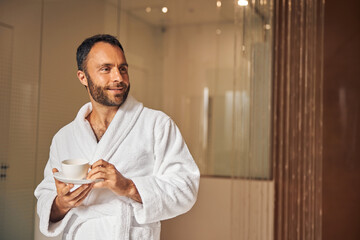 Joyful young man with coffee standing in spa salon