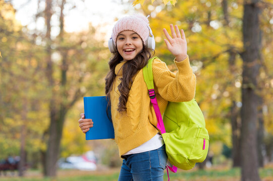 Enjoying the day. small girl wear headphones. back to school. modern education. child with backpack and book in forest. knowledge day. kid fall clothes fashion. happy kid walk in autumn park