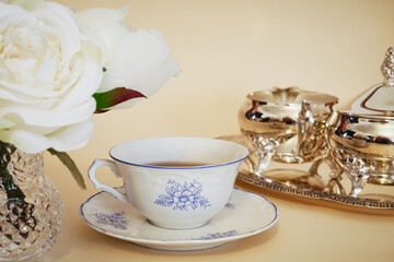 Roses bouquet, a fine porcelain china teacup and a silver tea set in a yellow background. Concept for afternoon tea