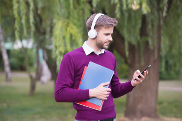 unshaven guy holding notebook and listening music in earphones from smartphone, education