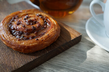 an appetizing bun with cinnamon, caramel and nuts on a wooden cutting board as a delicious breakfast with coffee or tea