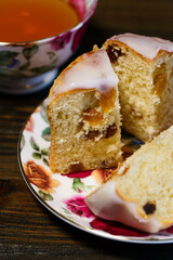 Traditional Easter kulich pastry served on colorful porcelain plate with cup of tea. Wooden table, high resolution